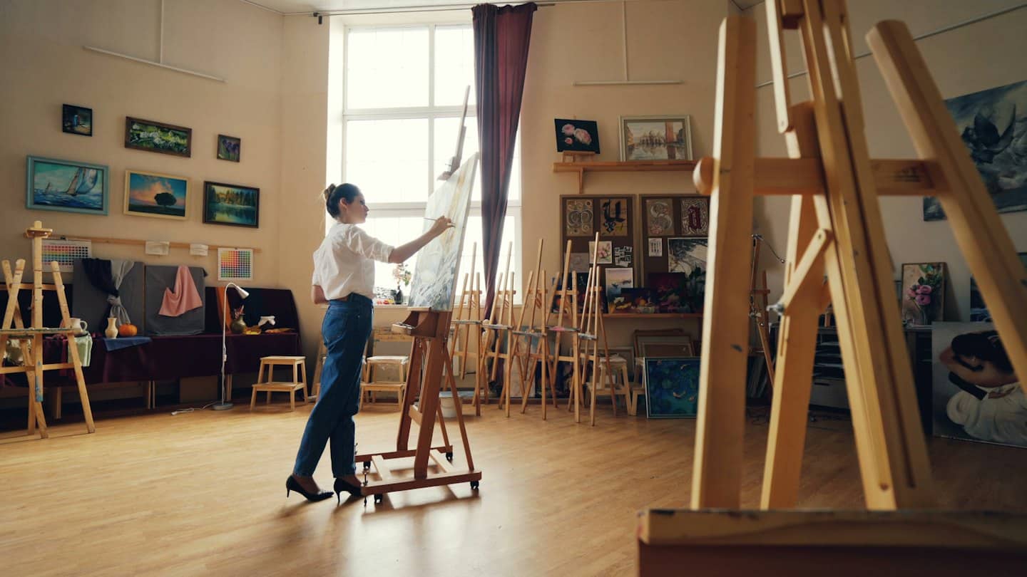 Donna che dipinge una grande tela in un luminoso studio d'arte.