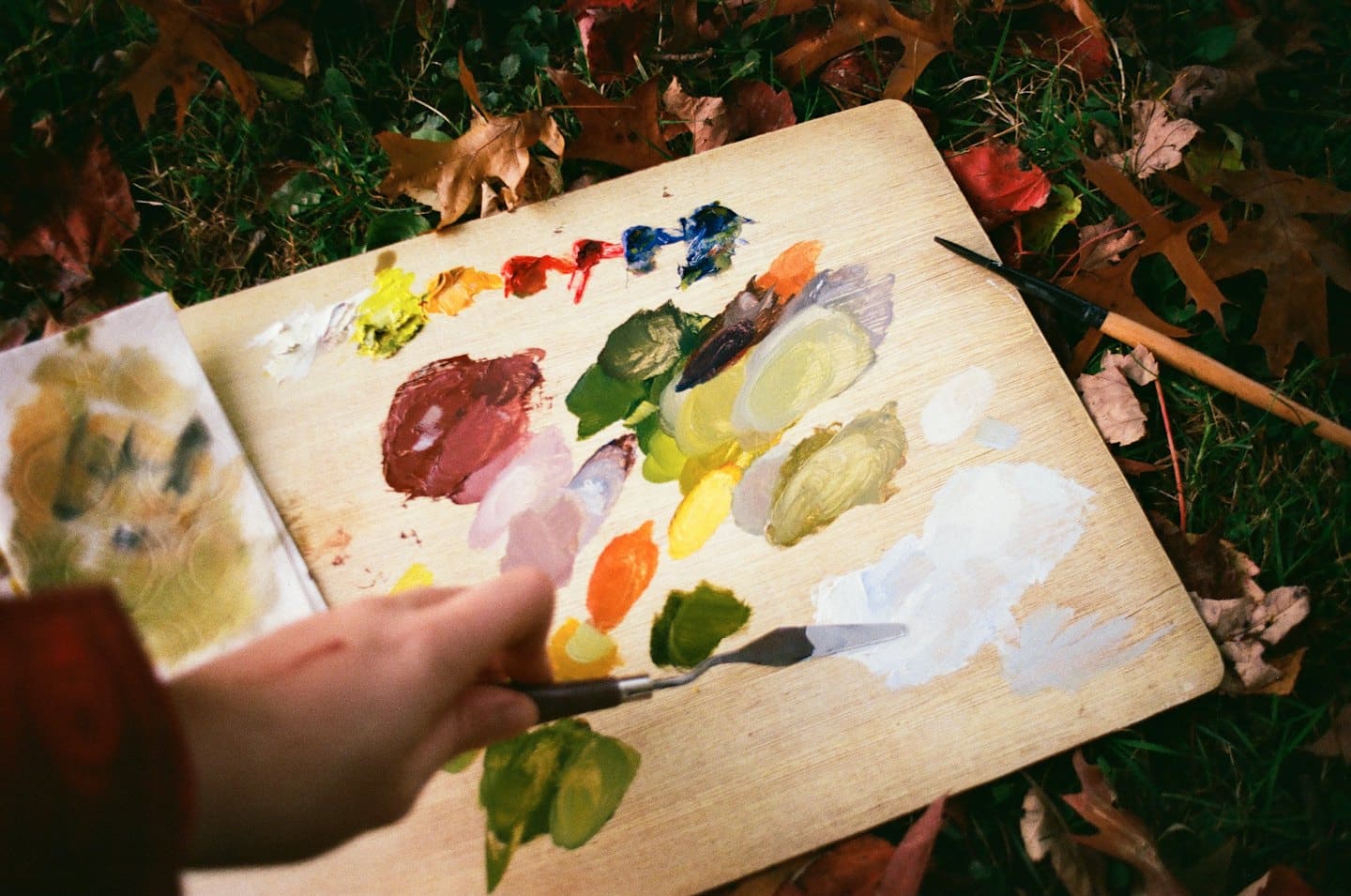 Una mano mescola colori vivaci su una tavolozza di legno all'aperto.