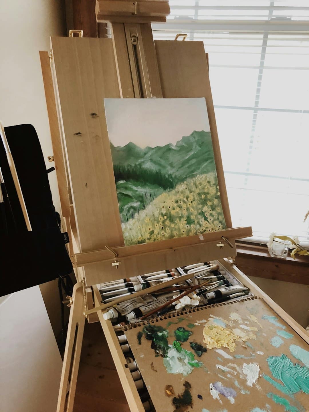 Cavalletto di legno con un dipinto di paesaggio e materiali artistici sottostanti.