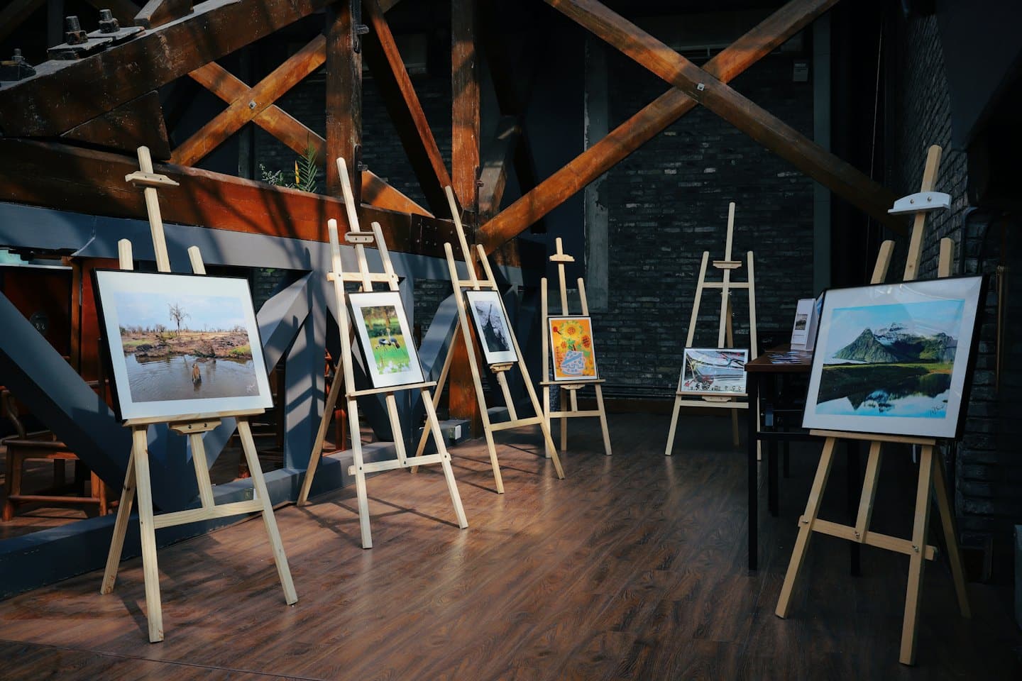 Mostra d'arte con opere incorniciate su cavalletti di legno.